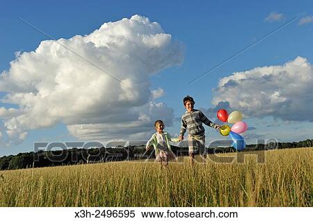 Stock Photography - young boy with his sister running with balloons in a field, Ile-de-France, France, Europe.. Fotosearch