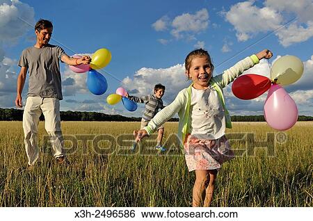 Stock Photograph - young father running with his children and balloons, Ile-de-France, France, Europe.. Fotosearch