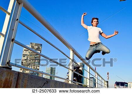 Young man jumping over an iron railing, blue sky. Barcelona, Catalonia, Spain. View Large Photo Image Stock Image - Young man jumping over an iron railing, blue sky. Barcelona, Catalonia, Spain.. Fotosearch