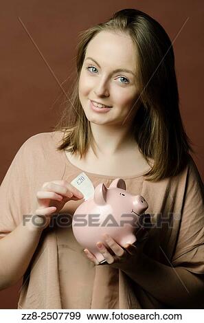 Stock Photo - Young woman saving a twenty pounds Sterling note in a piggy bank.. Fotosearch