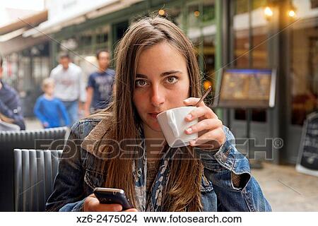 Young woman, with cell phone, drinking a coffee and looking at camera. View Large Photo Image Picture - Young woman, with cell phone, drinking a coffee and looking at camera.. Fotosearch