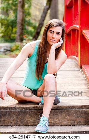 A 22 year old brunette woman looking directly at the camera sitting on a foot bridge in a garden setting. View Large Photo Image Stock Photo - A 22 year old brunette woman looking directly at the camera sitting on a foot bridge in a garden setting.. Fotosearch