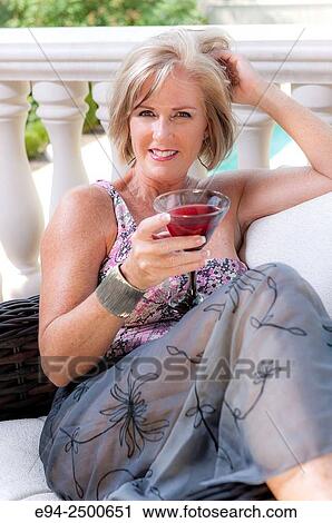 A smiling 56 year old blond woman in casual summer clothing lounging in a backyard, looking at the camera and holding a beverage. View Large Photo Image Stock Image - A smiling 56 year old blond woman in casual summer clothing lounging in a backyard, looking at the camera and holding a beverage.. Fotosearch