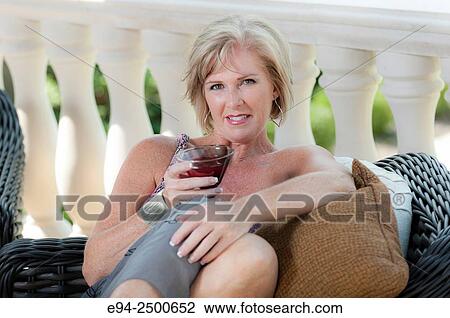 A smiling 56 year old blond woman in casual summer clothing lounging in a backyard, looking at the camera and holding a beverage. View Large Photo Image Stock Image - A smiling 56 year old blond woman in casual summer clothing lounging in a backyard, looking at the camera and holding a beverage.. Fotosearch