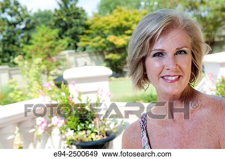A smiling 56 year old blond woman in casual summer clothing lounging in a backyard, looking at the camera. View Large Photo Image Stock Photo - A smiling 56 year old blond woman in casual summer clothing lounging in a backyard, looking at the camera.. Fotosearch