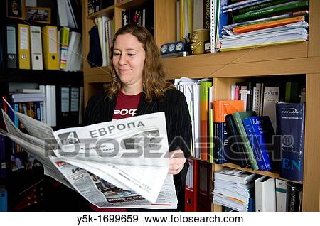 A young female professional reading a Russian newspaper in font of her library. View Large Photo Image Stock Photo - A young female professional reading a Russian newspaper in font of her library.. Fotosearch
