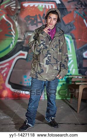 A young man with cigarette posing in front of a large graffity. View Large Photo Image Stock Photo - A young man with cigarette posing in front of a large graffity.. Fotosearch