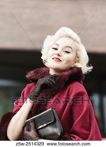 Stock Photo - Close up, fashionable blond posing and she wearing red coat, urban scene.. Fotosearch