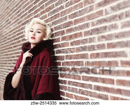 Stock Photography - Fashionable blond wearing red coat, brick wall on background, urban scene.. Fotosearch