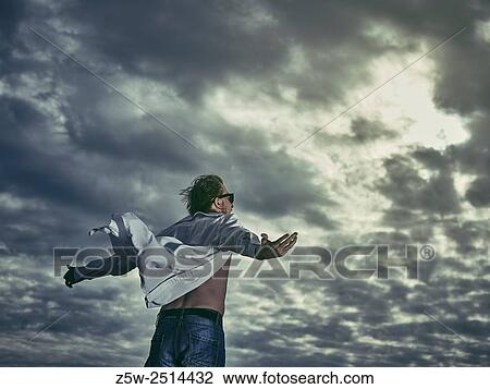 Stock Image - Handsome man wearing white shirt and jeans, he spread her arms and looks up to sky.. Fotosearch