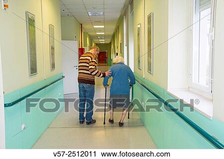 Mature man helping old woman walk along a corridor in a nursing home. View Large Photo Image Stock Image - Mature man helping old woman walk along a corridor in a nursing home.. Fotosearch