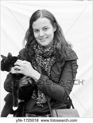Stock Photo - Portrait of a young woman with cat against white sheet background.. Fotosearch