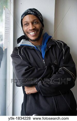 Stock Photo - Rotterdam, Netherlands A black Caribbean man looking out the window and smiling, while leaning against the wall. Fotosearch