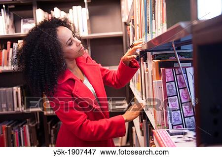 Rotterdam, Netherlands. Young, African woman, searching for a suitable book, between the bookshelves in a public library. View Large Photo Image Stock Photo - Rotterdam, Netherlands. Young, African woman, searching for a suitable book, between the bookshelves in a public library.. Fotosearch