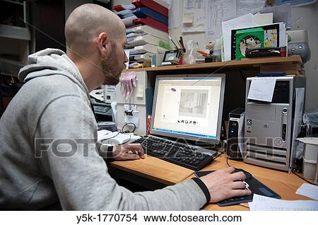 Picture - Rotterdam, Netherlands. Young professional working with a computer behind his office desk.. Fotosearch