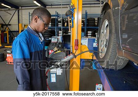 Tilburg, Netherlands. A mechanic or apprentice engineer, immigrated from the Caribbean islands to the Netherlands, in his workshop working on the regular, periodical maintenance of a car. View Large Photo Image Stock Photo - Tilburg, Netherlands. A mechanic or apprentice engineer, immigrated from the Caribbean islands to the Netherlands, in his workshop working on the regular, periodical maintenance of a car.. Fotosearch
