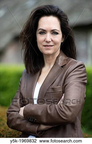 Stock Image - Tilburg, Netherlands. Successful middle-aged property broker in front of her refurbished farm in the rural area of Tilburg.. Fotosearch