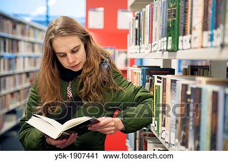 Tilburg, Netherlands. Young brunette reading a book in the public library, standing between the bookshelves with books. View Large Photo Image Stock Image - Tilburg, Netherlands. Young brunette reading a book in the public library, standing between the bookshelves with books.. Fotosearch