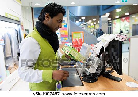 Tilburg, Netherlands. Young Indian male working at a cash register of a local supermarket, helping out customers with their groceries. View Large Photo Image Stock Photo - Tilburg, Netherlands. Young Indian male working at a cash register of a local supermarket, helping out customers with their groceries.. Fotosearch