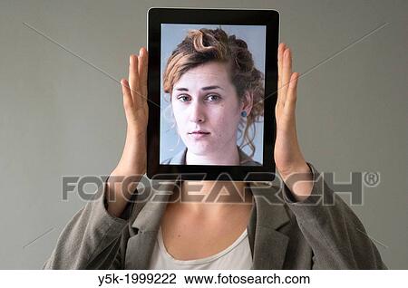 Tilburg, Netherlands. Young woman holding up an Digital Tablet, showing her portrait, which was taken earlier, in front of her face. View Large Photo Image Stock Image - Tilburg, Netherlands. Young woman holding up an Digital Tablet, showing her portrait, which was taken earlier, in front of her face.. Fotosearch