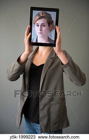 Tilburg, Netherlands. Young woman holding up an Digital Tablet, showing her portrait, which was taken earlier, in front of her face. View Large Photo Image Stock Image - Tilburg, Netherlands. Young woman holding up an Digital Tablet, showing her portrait, which was taken earlier, in front of her face.. Fotosearch