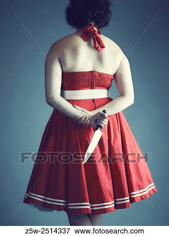 Stock Photo - Woman hide a bread knife behind her back, cross-processed studio shot.. Fotosearch