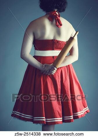 Stock Photo - Woman hide a rolling pin behind her back, cross-processed studio shot.. Fotosearch