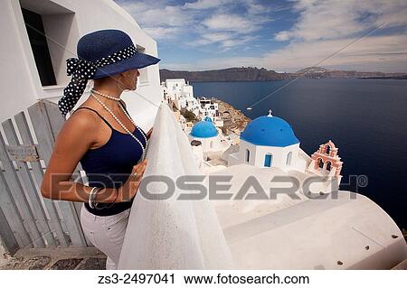 Stock Image - Woman in front of a blue domed church in Oia town with a ferry at the background, Santorini, Cyclades Islands, Greek Islands, Greece, Europe.. Fotosearch