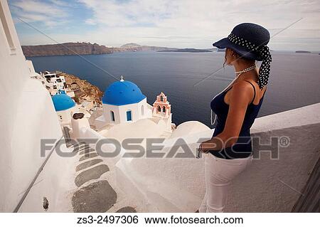 Stock Photograph - Woman in front of a blue domed church, Oia town, Santorini, Cyclades Islands, Greek Islands, Greece, Europe.. Fotosearch