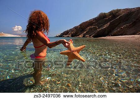 Woman in the sea with a starfish in her hand at Agios Georgios beach, Folegandros, Cyclades Islands, Greek Islands; Greece, Europe. View Large Photo Image Stock Photograph - Woman in the sea with a starfish in her hand at Agios Georgios beach, Folegandros, Cyclades Islands, Greek Islands; Greece, Europe.. Fotosearch