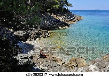 young woman sitting on rocks at a creek of Mrcara islet in the north-west of Lastovo island, Croatia, Southeast Europe. View Large Photo Image Stock Photo - young woman sitting on rocks at a creek of Mrcara islet in the north-west of Lastovo island, Croatia, Southeast Europe.. Fotosearch