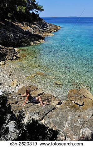 Stock Photo - young woman sitting on rocks at a creek of Mrcara islet in the north-west of Lastovo island, Croatia, Southeast Europe.. Fotosearch