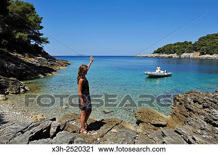 Stock Image - young woman standing on rocks at a creek of Mrcara islet at the north-west of Lastovo island, Croatia, Southeast Europe.. Fotosearch