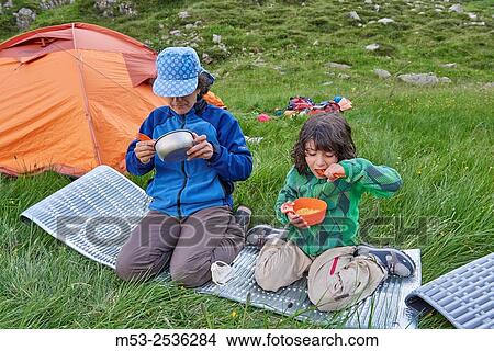 Picture - A mother with her 5 years old daughter have a meal nearby their camp site.. Fotosearch