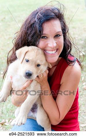 A smiling 38 year old brunette woman looking at the camera and holding a young puppy on a farm. View Large Photo Image Stock Image - A smiling 38 year old brunette woman looking at the camera and holding a young puppy on a farm.. Fotosearch