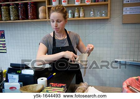 Amsterdam, Netherlands. A young woman is wrapping up a lunch-order for a customer, meanwhile punching in the cash-register. View Large Photo Image Stock Image - Amsterdam, Netherlands. A young woman is wrapping up a lunch-order for a customer, meanwhile punching in the cash-register.. Fotosearch