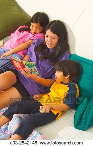An Asian American teen baby sitter reads to her infant sister and younger brother in bed at home in Laguna Beach, CA. View Large Photo Image Stock Photography - An Asian American teen baby sitter reads to her infant sister and younger brother in bed at home in Laguna Beach, CA.. Fotosearch
