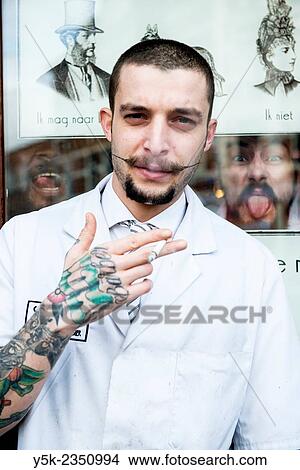 Barber store Schorem, Rotterdam, Netherlands. Portrait of a barber with tattoos on his arm, smoking a cigarette just outside the front door. View Large Photo Image Picture - Barber store Schorem, Rotterdam, Netherlands. Portrait of a barber with tattoos on his arm, smoking a cigarette just outside the front door.. Fotosearch