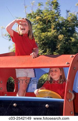 Stock Photo - Eight year old identical twin girls play on a toy car in a Laguna Niguel, CA, park. MODEL RELEASE.. Fotosearch