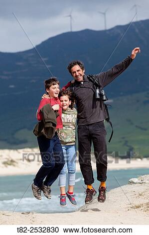 Stock Image - father and two happy children jumping. Cadiz, Andalusia, Spain. Fotosearch