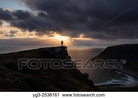 Female hiker watches midnight sun over sea from Nonstind mountain peak, Vestvågøy, Lofoten Islands, Norway. View Large Photo Image Stock Image - Female hiker watches midnight sun over sea from Nonstind mountain peak, Vestvågøy, Lofoten Islands, Norway.. Fotosearch