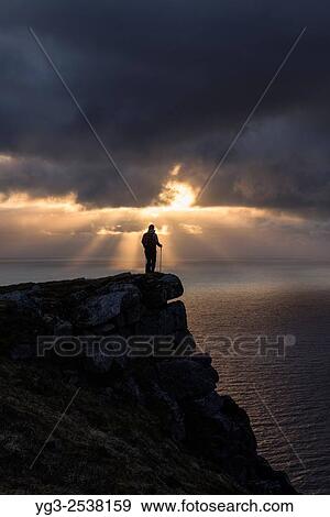 Female hiker watches midnight sun over sea from Nonstind mountain peak, Vestvågøy, Lofoten Islands, Norway. View Large Photo Image Stock Photo - Female hiker watches midnight sun over sea from Nonstind mountain peak, Vestvågøy, Lofoten Islands, Norway.. Fotosearch