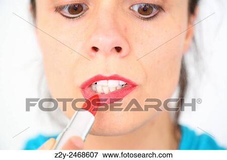 Stock Photo - Girl painting her lips with eyes looking down.. Fotosearch