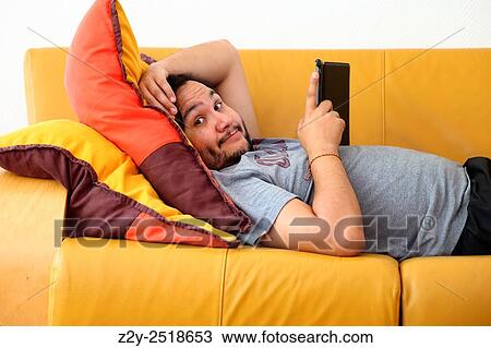 Man laying on a yellow couch with ipad in his hands and looking at the camera. View Large Photo Image Stock Image - Man laying on a yellow couch with ipad in his hands and looking at the camera.. Fotosearch