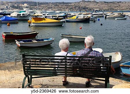 mature couple sitting at the bench admiring view of St Paul Bay, Malta. View Large Photo Image Stock Photograph - mature couple sitting at the bench admiring view of St Paul Bay, Malta.. Fotosearch