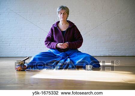 Stock Image - Older woman, meditating in an empty room, using Buddhist techniques.. Fotosearch