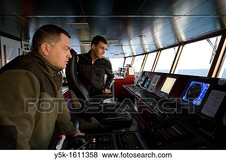Stock Photo - On the bridge of the MV Flintercape a Russian first-officer and a Dutch Cadet study the onboard instruments, during their voyage from Rotterdam, Netherlands to Sundsvall, Sweden.. Fotosearch