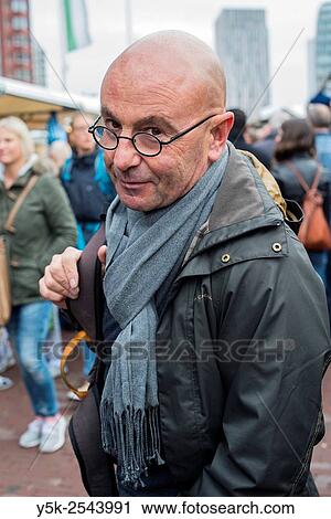 Stock Image - Rotterdam, Netherlands. Middle aged bald male wearing glasses looking back, while standing in a crowd on the weekly Saturday market.. Fotosearch