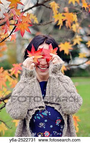 Stock Image - Smiling mid adult woman holding leaf close to her face, autumn. Fotosearch