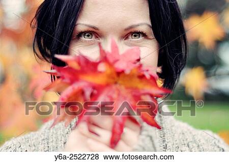 Stock Photo - Smiling mid adult woman holding leaf close to her face.. Fotosearch